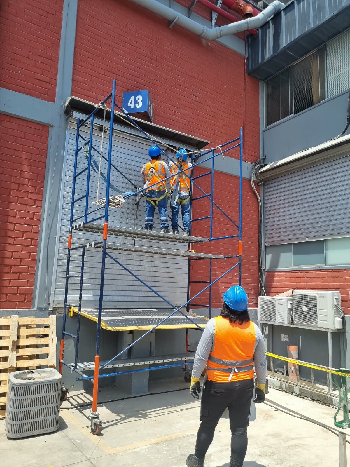 Cuadrilla en andamio realizando mantenimiento de puerta enrollable